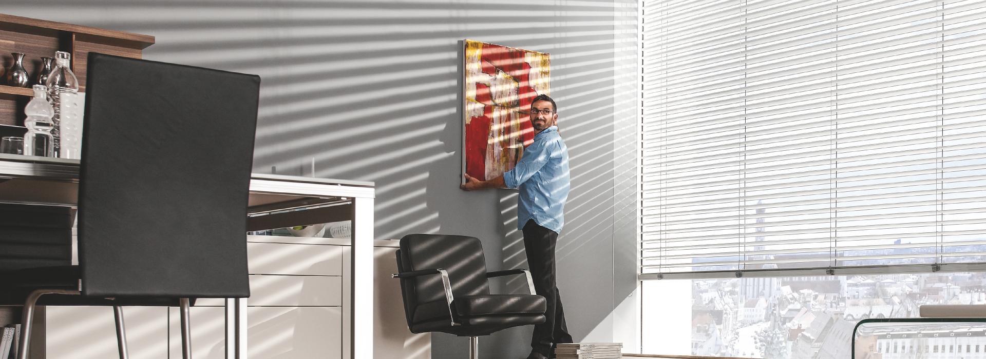 Homme accroche un tableau au mur du bureau, brise-soleil inclinés