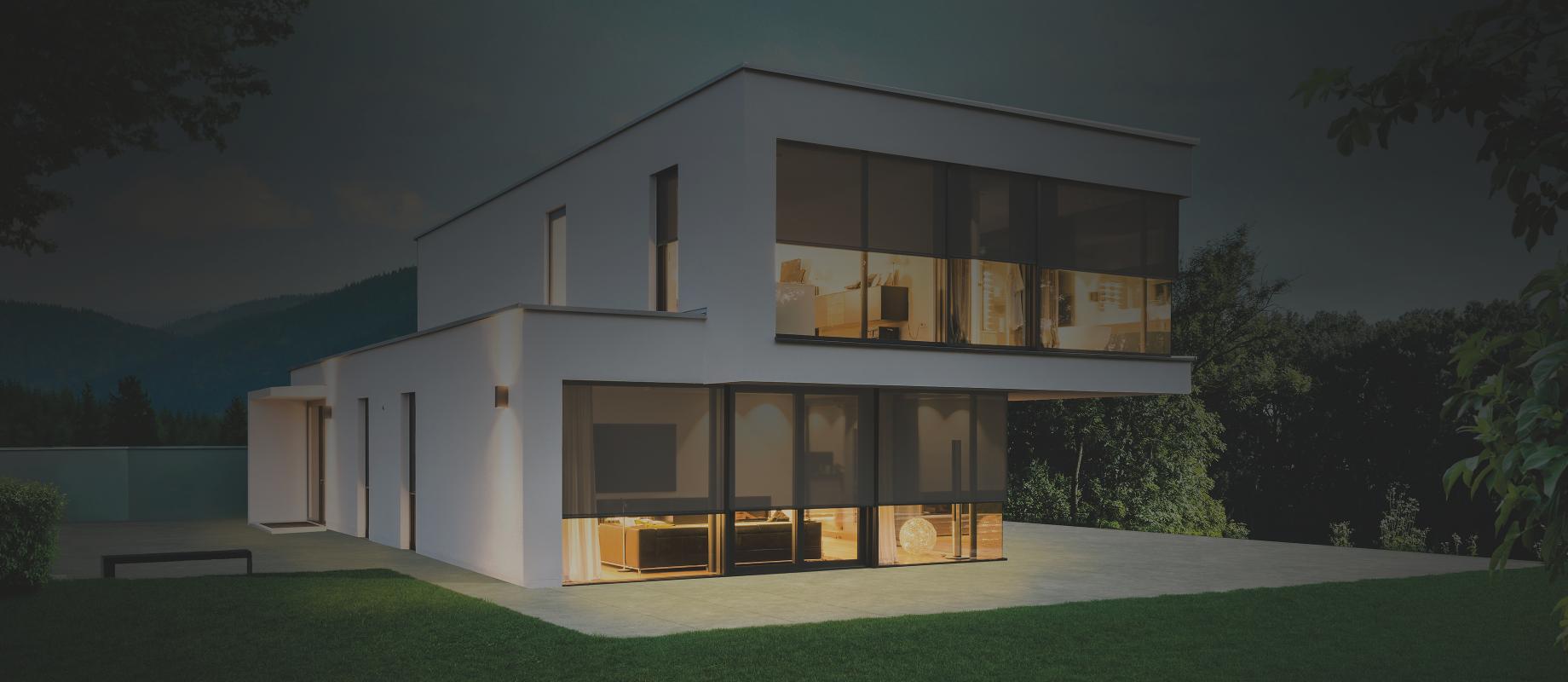 Maison témoin moderne, au crépuscule, éclairée de l'intérieur, stores toiles