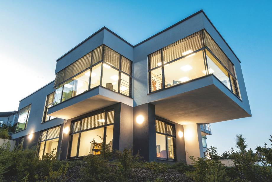 Immeuble de bureaux en pente, au crépuscule, éclairé de l'intérieur, brise-soleil