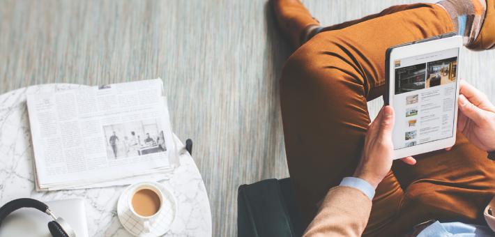Homme est assis dans le fauteuil en tenant une tablette dans les mains - À côté du fauteuil, il y a une table avec du café, un journal et des écouteurs