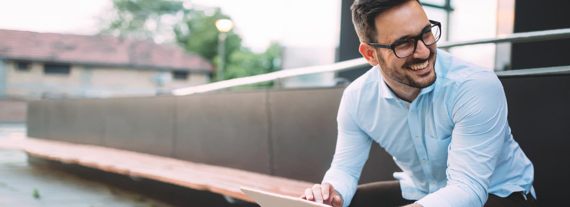 Un jeune homme est assis sur un banc avec une tablette et rit