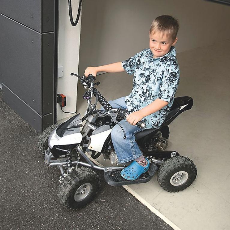 Portes de garage ROMA - Arrêt de sécurité automatique Un garçon passe avec son quad sous la porte de garage. Celle-ci stoppe grâce à l'arrêt de sécurité automatique.