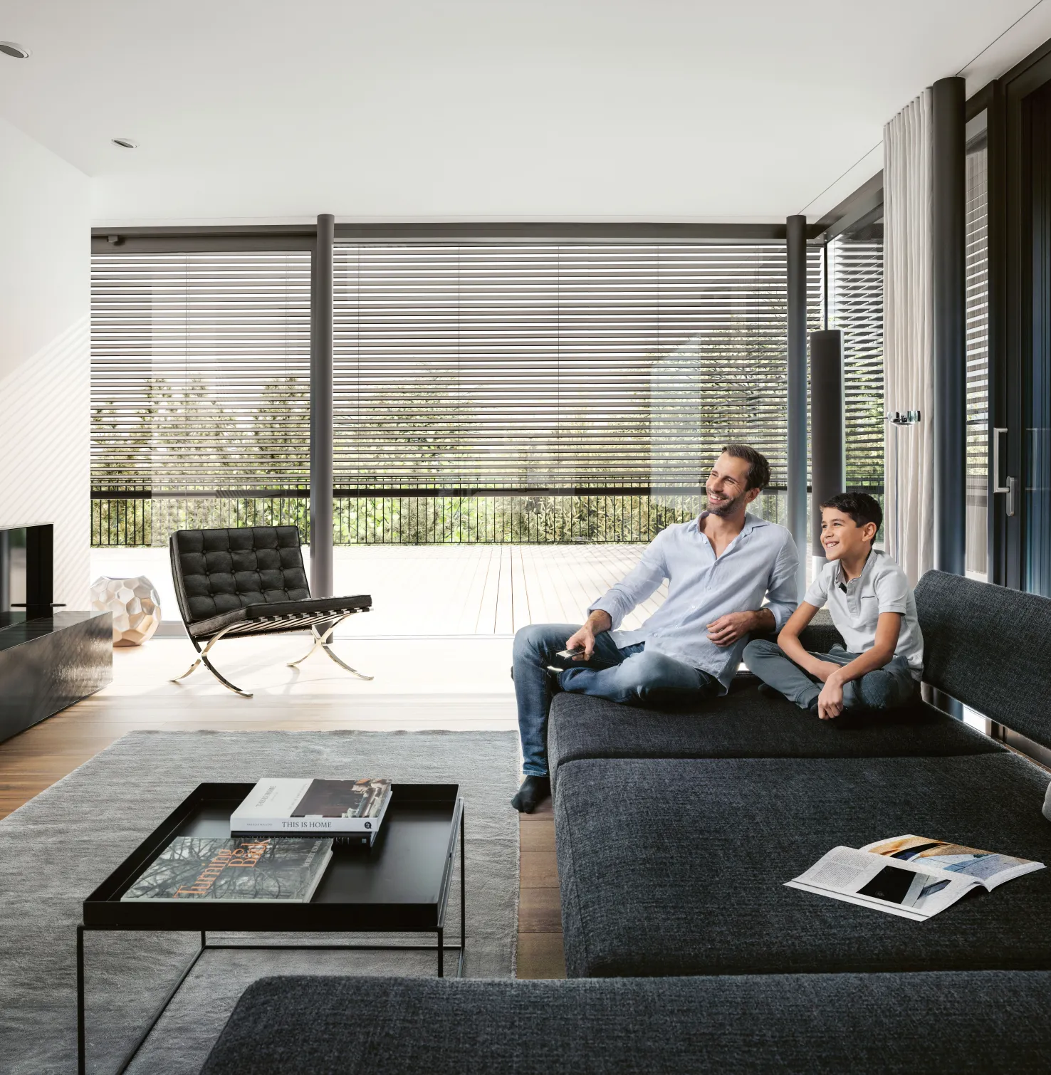 Salon avec canapé et père et fils avec Brise-soleil orientables, également stores extérieurs, devant la fenêtre