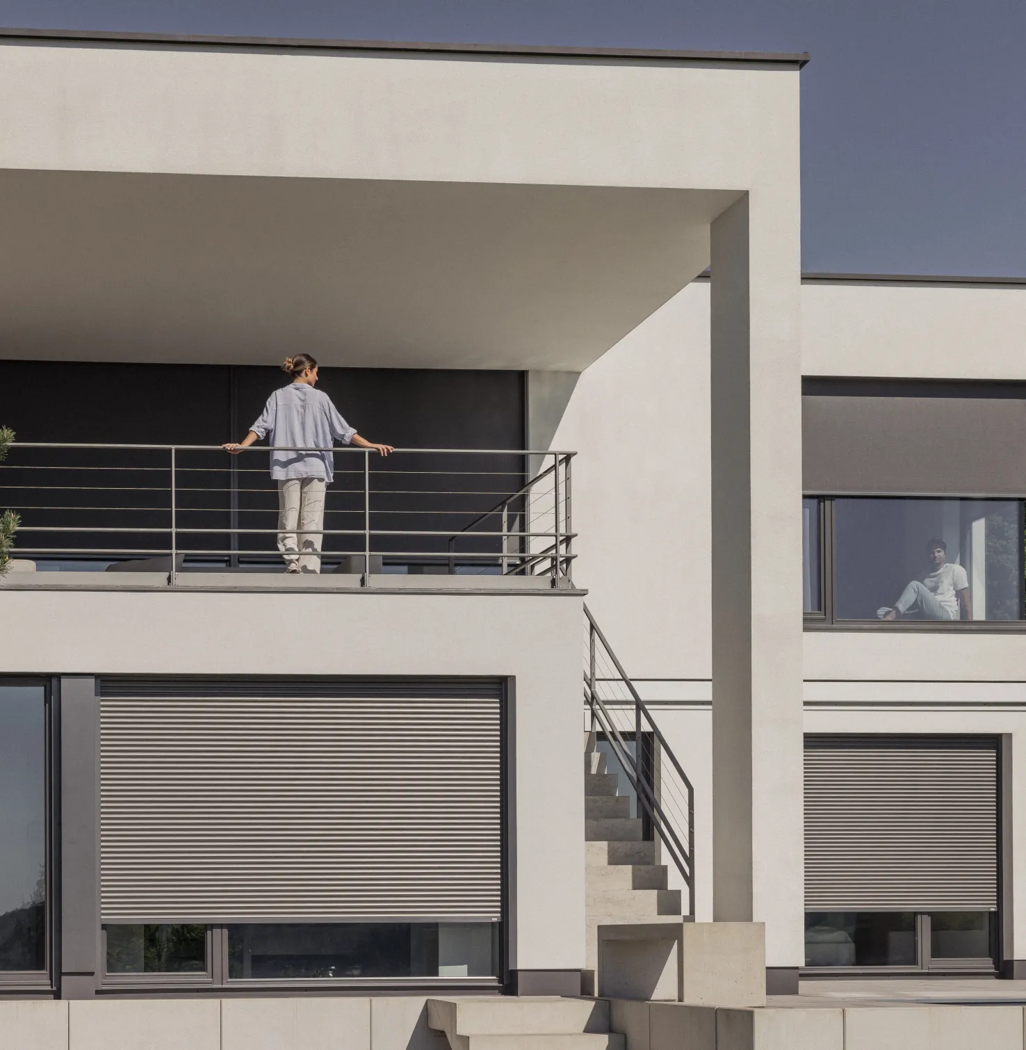 Maison avec volets roulants et Stores toiles avec une femme sur le balcon